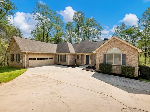 Single story home with a garage, driveway, a shingled roof, and brick siding