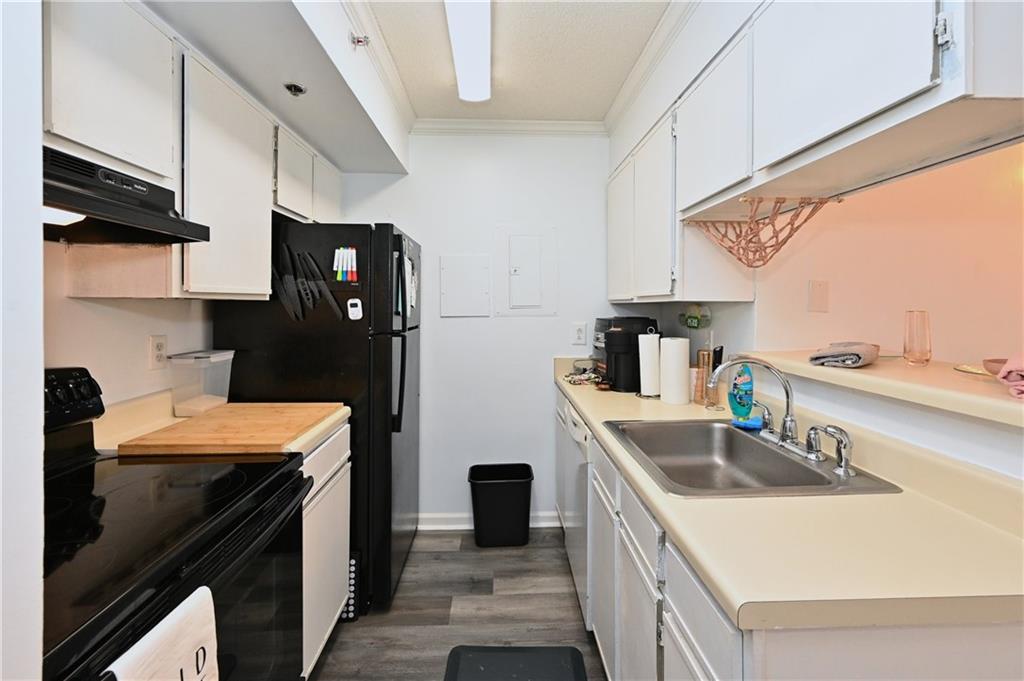 Kitchen with crown molding, dark wood-type flooring, white cabinetry, sink, and electric range