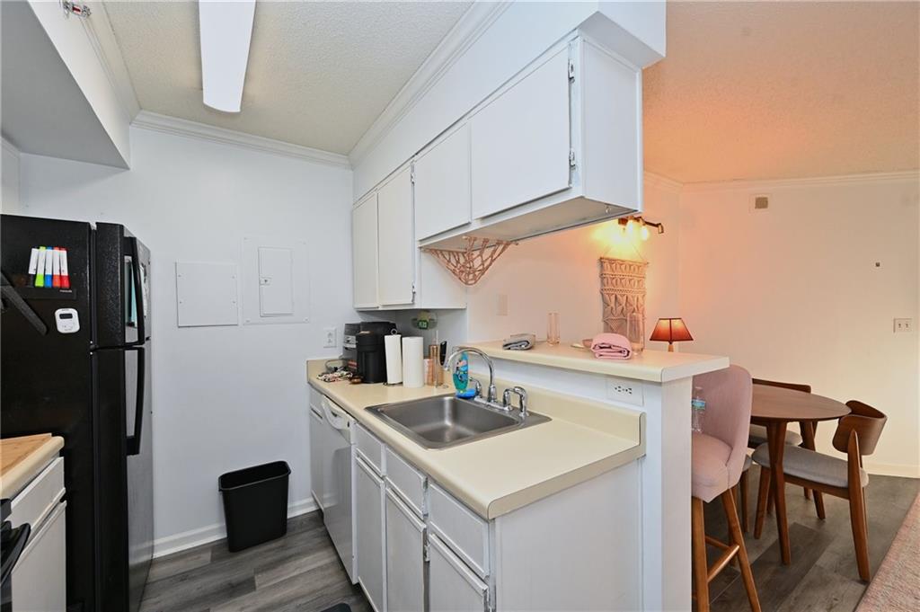 Kitchen featuring ornamental molding, black refrigerator, white cabinets, sink, and dark wood-type flooring