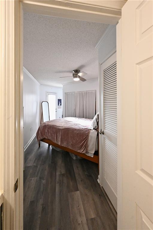 Bedroom with a closet, a textured ceiling, crown molding, dark hardwood / wood-style floors, and ceiling fan