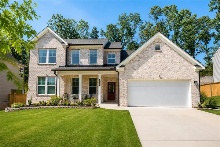 Two-story light brick exterior featuring a covered entry porch, a gabled roofline, an attached two-car garage, and a concrete driveway