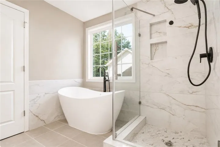 Freestanding soaking tub with a floor-mounted faucet, walk-in shower with glass enclosure, white marble-look tile, and dual shower heads
