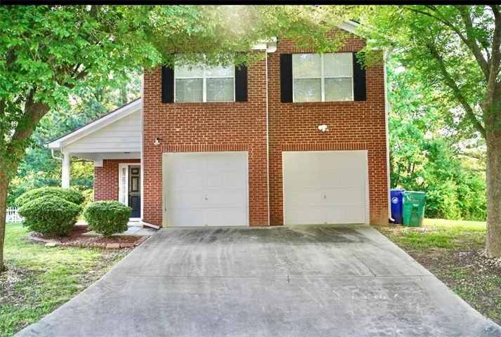 Brick exterior with white siding accents, two single-car garages, a covered front entry, and mature landscaping