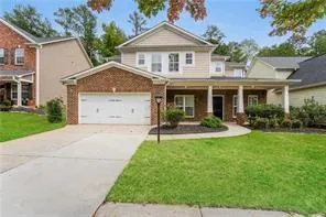Brick and siding exterior, front-facing two-car garage, covered porch with white columns, concrete driveway, and manicured lawn