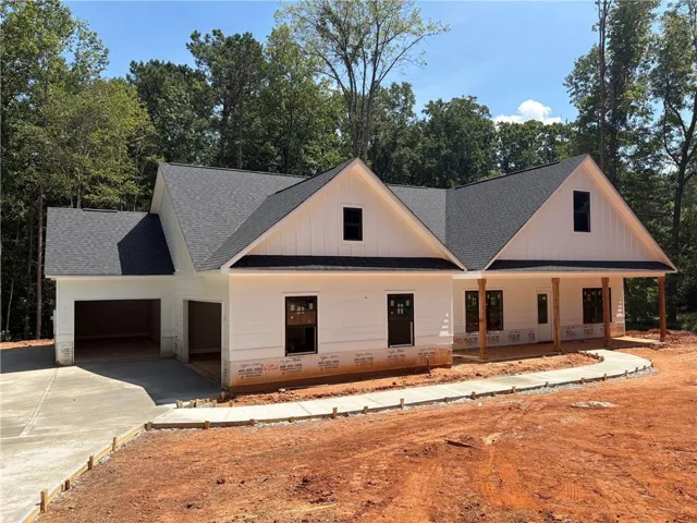 Modern farmhouse exterior with white vertical siding, a dark shingle roof, an attached two-car garage, and a covered front porch with natural wood posts