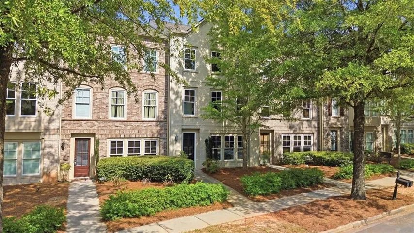 Brick and stucco exterior with multiple windows, a paved walkway, and maintained landscaping