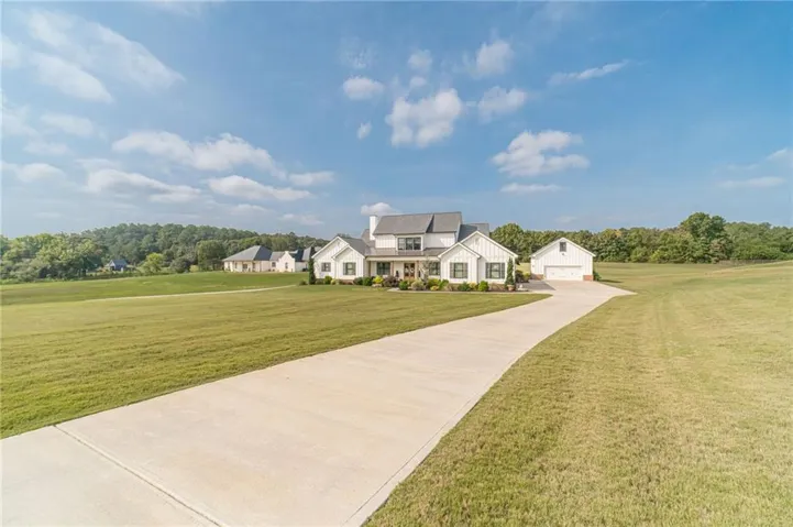 White exterior with dark trim accents, concrete drive, attached garage, detached garage, and expansive green lawns