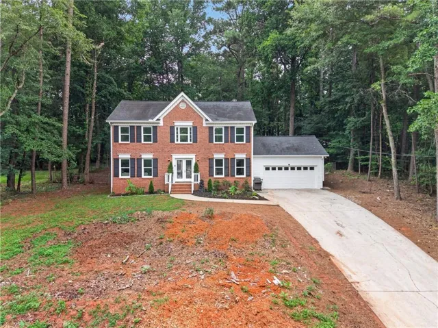 Brick facade home featuring a prominent two-story entry, white-framed windows with dark shutters, an attached garage, and a concrete driveway
