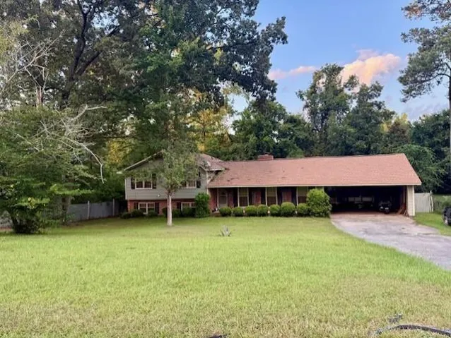 Split-level residence featuring brick and siding exterior, an attached carport, a shingle roof, and established landscaping