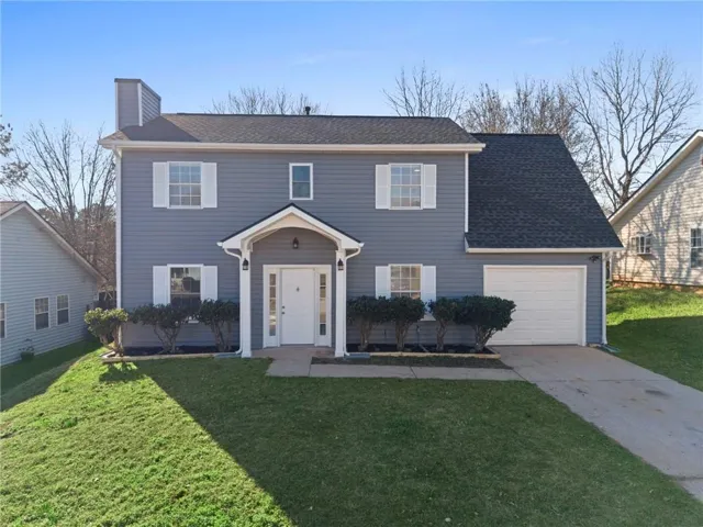 Colonial house featuring a front lawn, a chimney, a garage, concrete driveway, and roof with shingles