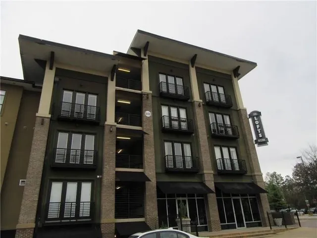 Multi-story building featuring a brick and stucco exterior, multiple Juliette balconies with black railings, and ground-level commercial awnings