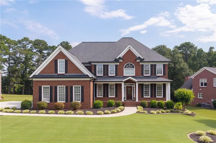 Traditional brick exterior with white trim, a dark shingle roof, a curving concrete walkway, and landscaped garden beds