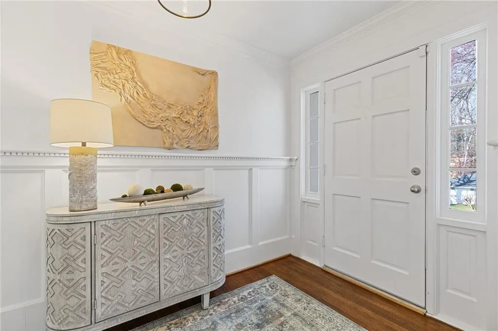 Foyer with dark wood finished floors, ornamental molding, wainscoting, and a decorative wall