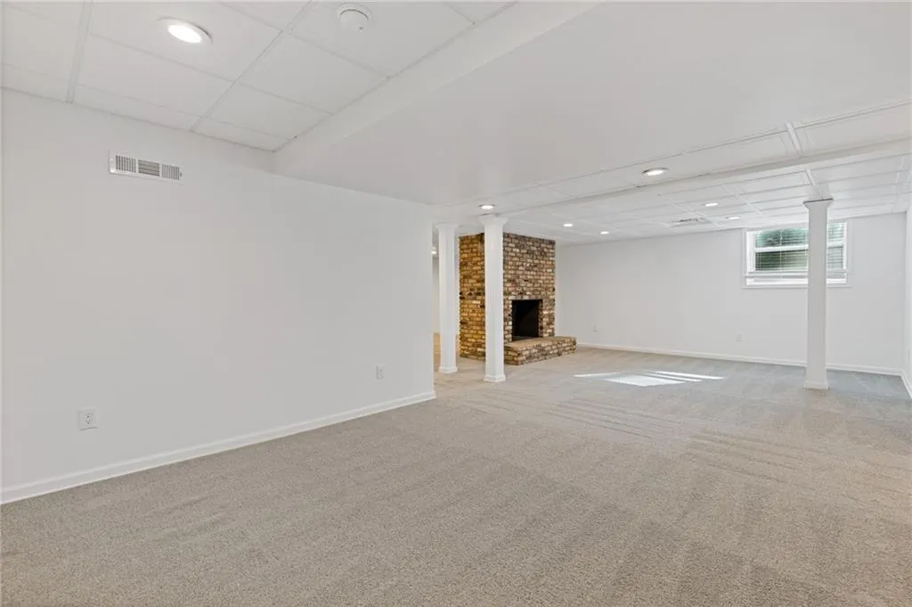 Basement with visible vents, a brick fireplace, baseboards, a drop ceiling, and light colored carpet