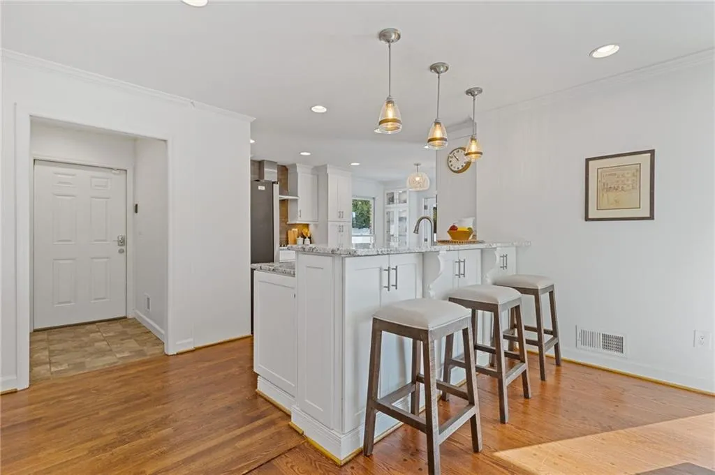 Kitchen featuring a breakfast bar area, a peninsula, light wood-style flooring, white cabinetry, and crown molding