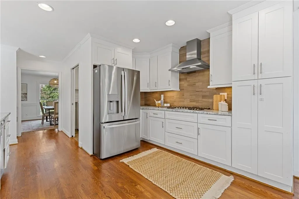 Kitchen with backsplash, wood finished floors, stainless steel appliances, wall chimney exhaust hood, and white cabinets