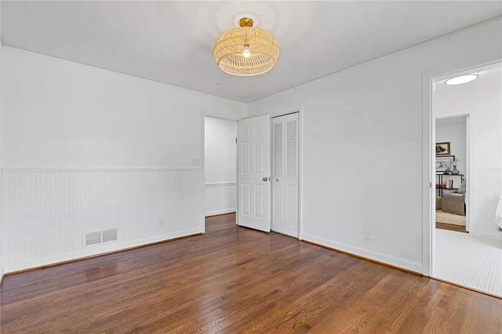 Unfurnished bedroom with a wainscoted wall, crown molding, wood finished floors, and visible vents