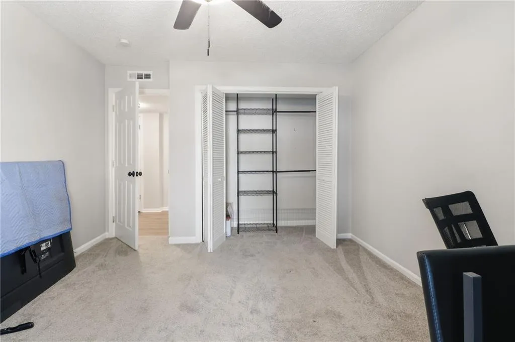 Neutral tone wall color, light gray carpeting, bi-fold louvered closet doors, built-in wire shelving, and a ceiling fan with light fixture