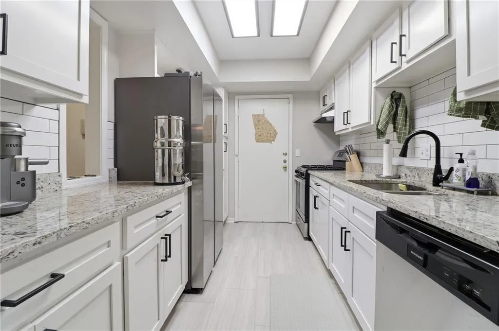 Galley kitchen featuring white shaker cabinetry with black hardware, granite-style countertops, and a subway tile backsplash