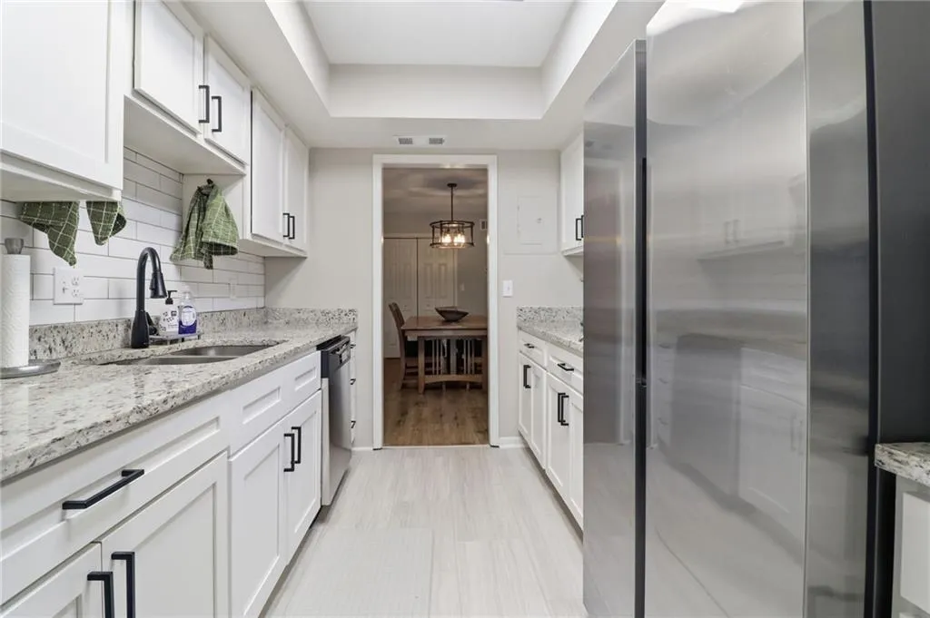 Galley kitchen featuring white cabinetry with matte black hardware, stone countertops, a subway tile backsplash, stainless steel appliances, and light wood-finish flooring