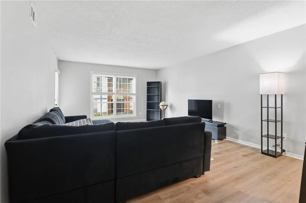 Bright living space featuring light wall paint, wood-finish flooring, and a large window with white blinds