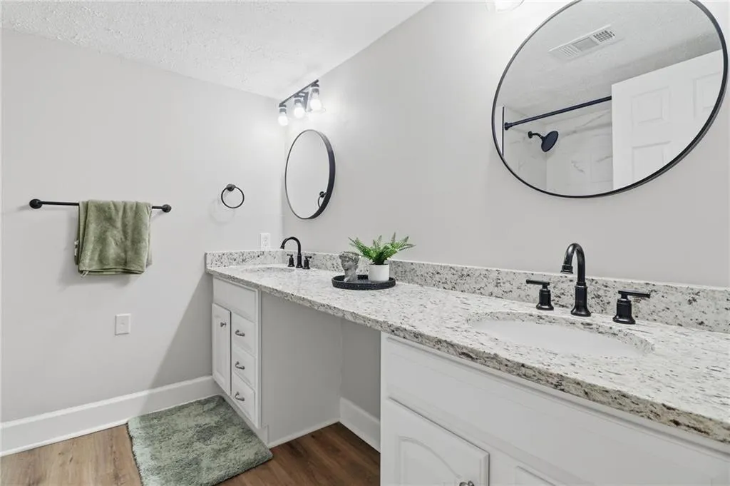 Bathroom featuring a dual vanity with white cabinetry, speckled countertops, undermount sinks, and matte black fixtures