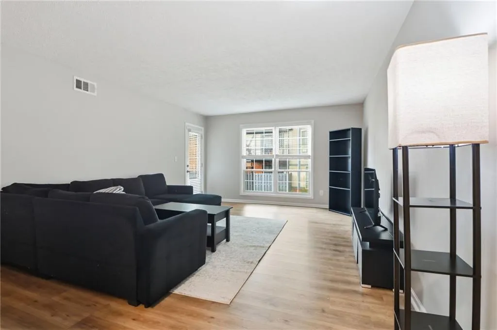 Bright living area with wood-finish flooring, light grey wall tones, and a rear window with white framing