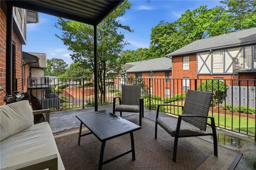 Covered patio with textured concrete flooring, black metal railing, and brick exterior
