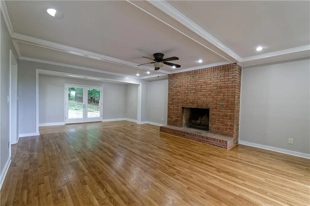 Unfurnished living room featuring ornamental molding, ceiling fan, a brick fireplace, wood finished floors, and baseboards