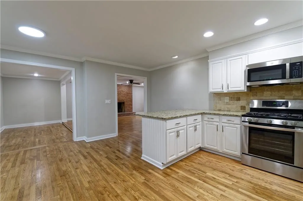 Kitchen featuring stainless steel appliances, white cabinetry, a peninsula, light wood-type flooring, and tasteful backsplash