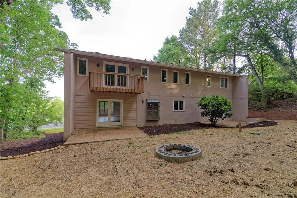 Rear view of property with a balcony, stucco siding, a fire pit, and a patio