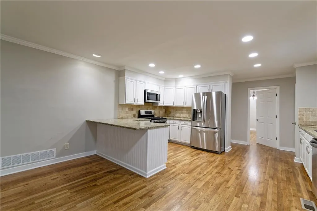 Kitchen with appliances with stainless steel finishes, decorative backsplash, white cabinetry, a peninsula, and crown molding
