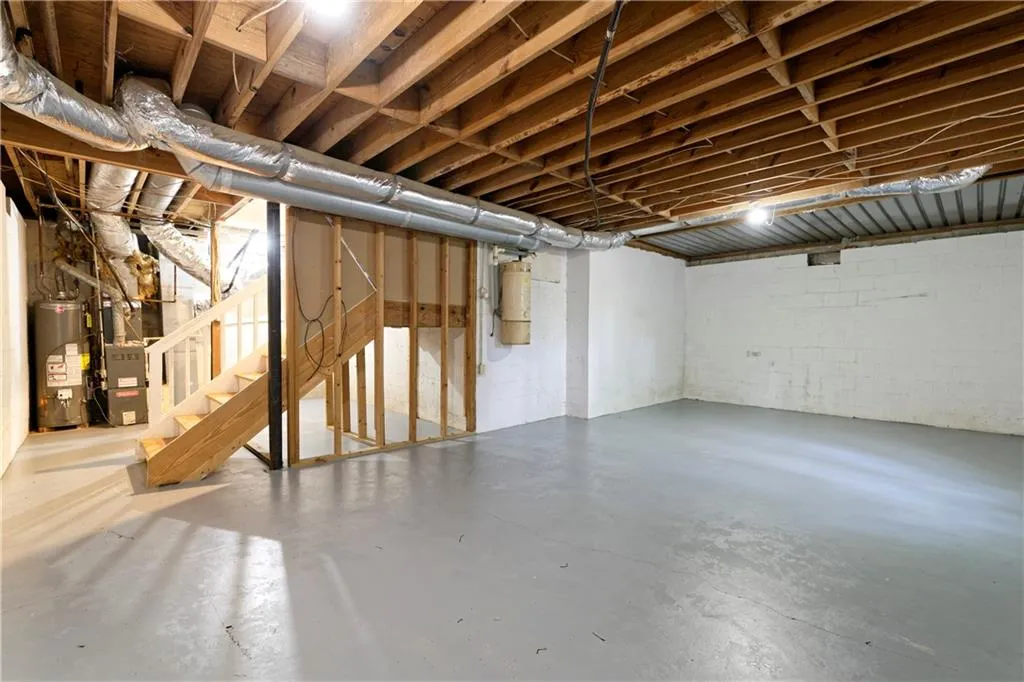 Unfinished basement with water heater, stairs, concrete block wall, and heating unit