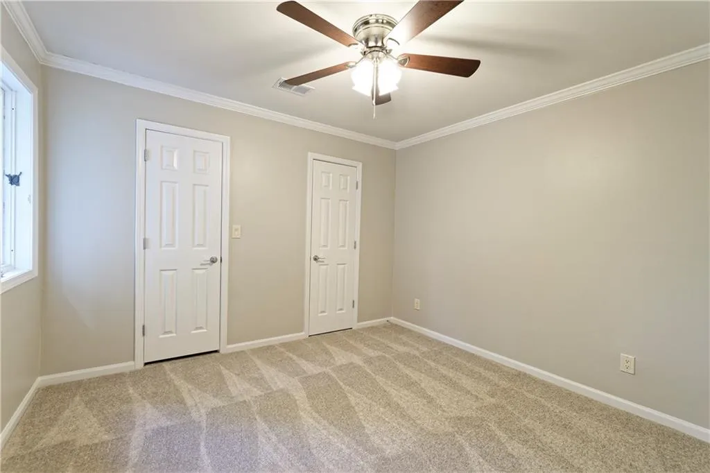 Unfurnished bedroom with ornamental molding, baseboards, light carpet, and a ceiling fan