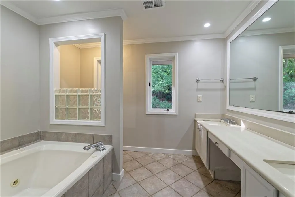 Bathroom with a tub with jets, double vanity, baseboards, ornamental molding, and recessed lighting
