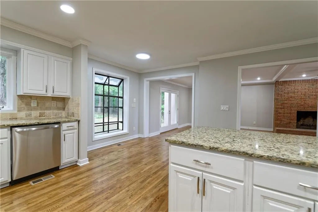 Kitchen featuring dishwasher, light wood-type flooring, ornamental molding, backsplash, and white cabinetry