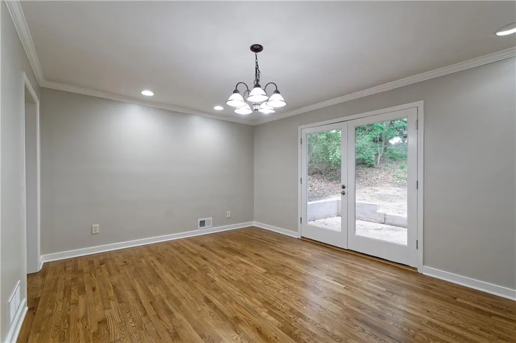 Unfurnished room featuring crown molding, wood finished floors, a chandelier, french doors, and baseboards