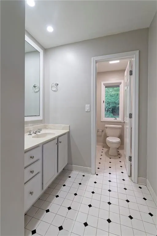 Bathroom featuring toilet, vanity, baseboards, tile patterned flooring, and recessed lighting