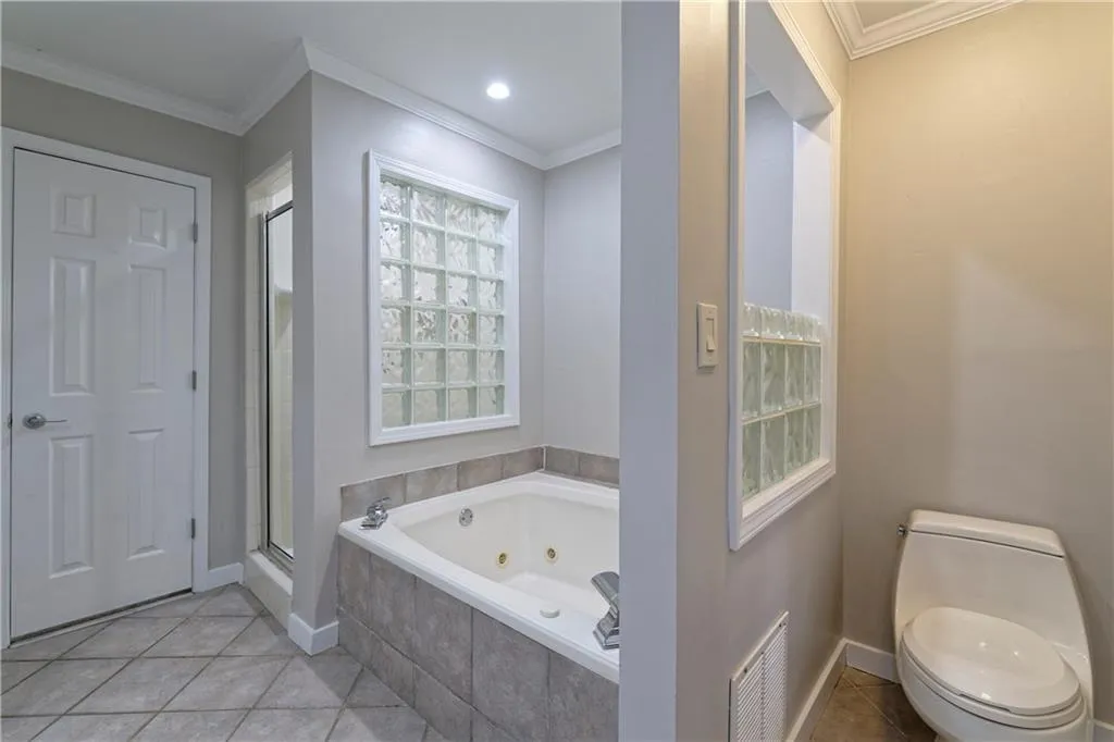 Full bath with a whirlpool tub, a stall shower, tile patterned floors, toilet, and ornamental molding
