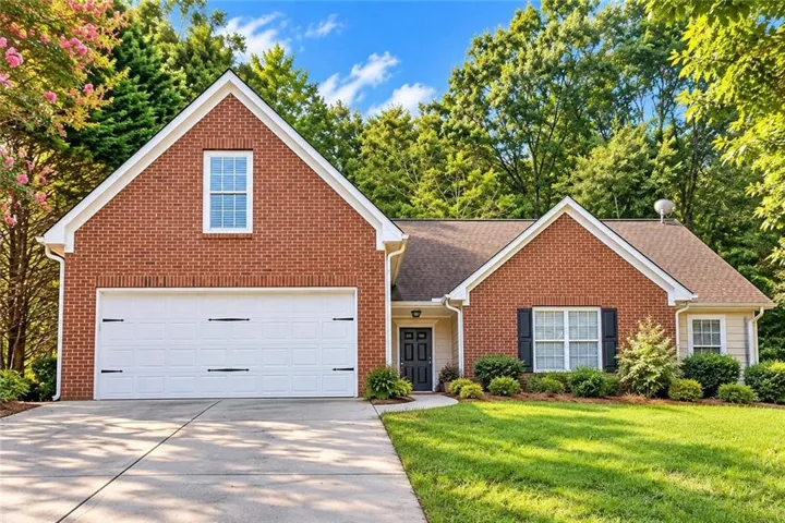 Red brick exterior with white trim, a two-car garage, a concrete driveway, and mature landscaping
