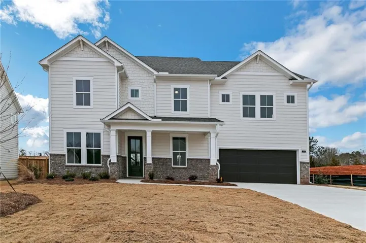 Two-story residence featuring white siding, stone accents, a covered entry porch with columns, a dark panel garage door, and a concrete driveway