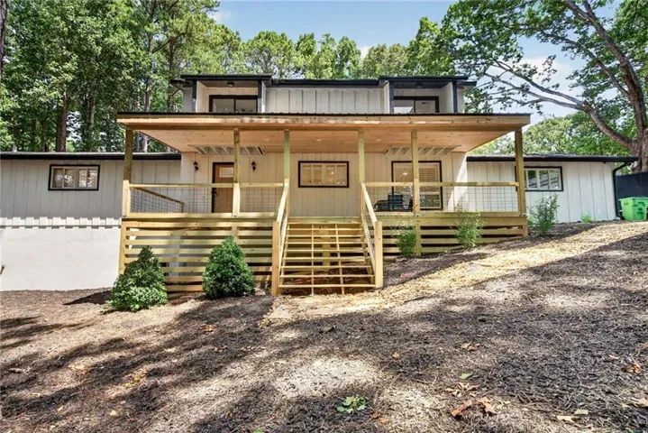 Board-and-batten siding with black-framed windows, a covered front porch featuring a natural wood ceiling, and a multi-level deck with wood stairs