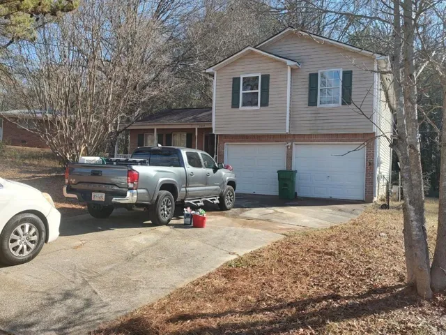 Two-story siding exterior with brick accents, featuring two garage doors, two front-facing windows with dark shutters, and a concrete driveway