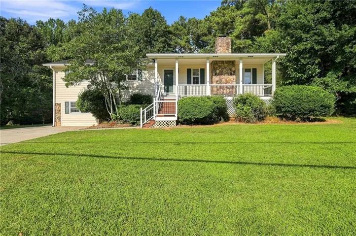 Property featuring a stone-clad chimney, an inviting front porch with white railings, and a broad grassy lawn