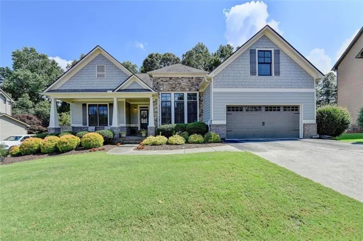 Craftsman-style exterior featuring a covered front porch, stone accents, shingle siding, a two-car garage, and a concrete driveway