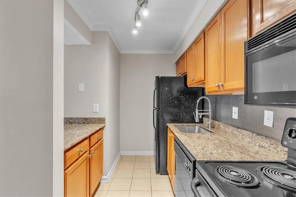 Kitchen with black appliances, ornamental molding, light stone counters, wood finish cabinetry, and backsplash