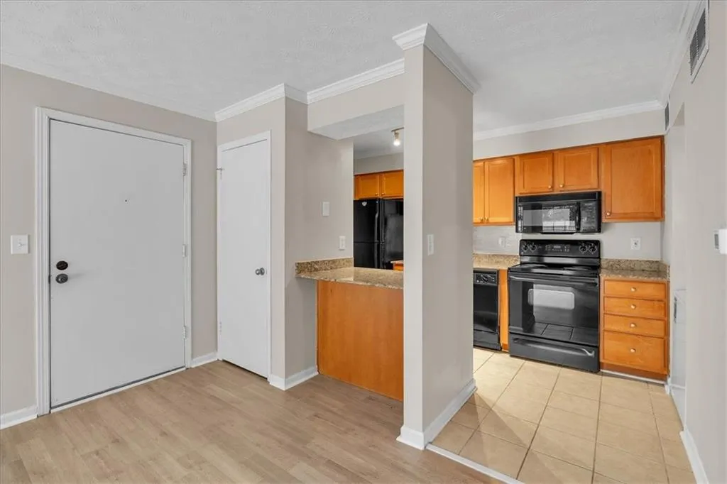 Kitchen featuring black appliances, wood finish cabinetry, light stone countertops, ornamental molding, and light wood-style flooring
