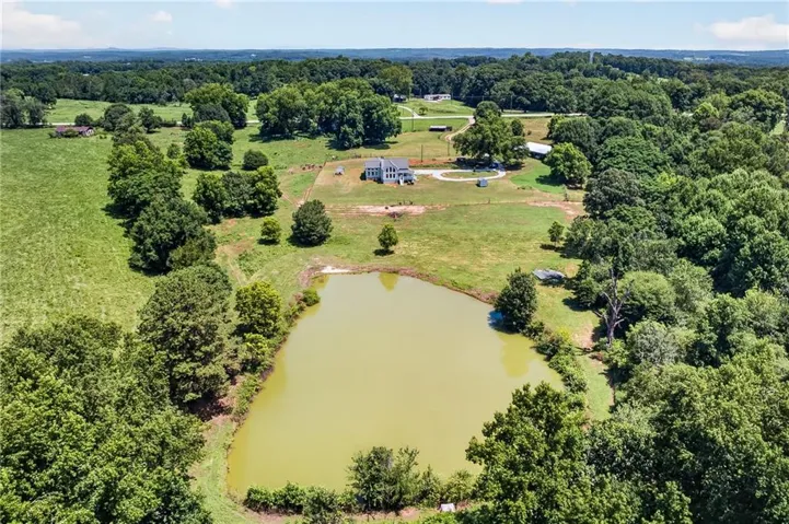 Expansive property featuring a large pond, extensive green space, mature trees, and a distant residence