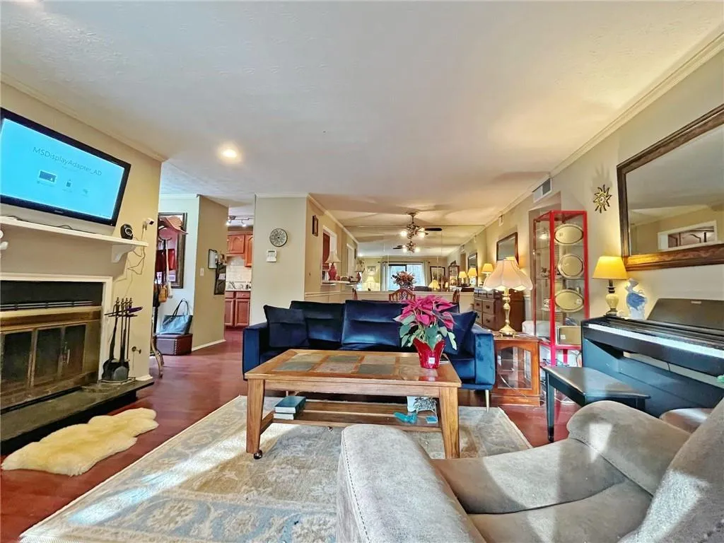 Living room with a glass covered fireplace, wood finished floors, ornamental molding, a ceiling fan, and a textured ceiling