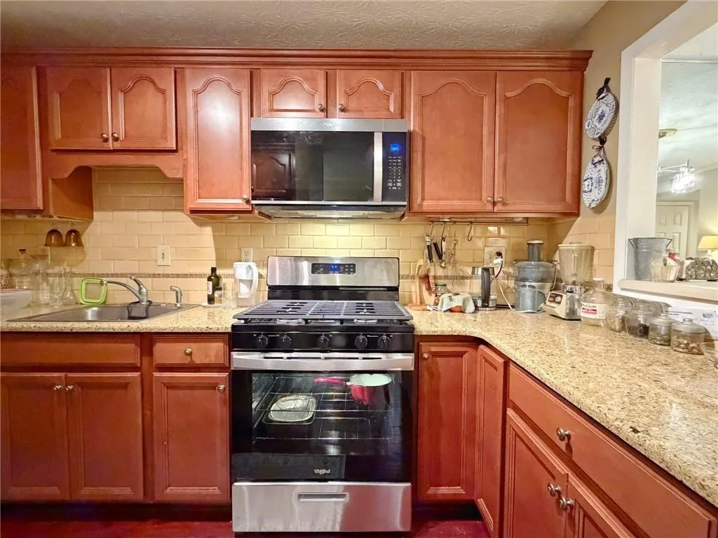 Kitchen with stainless steel appliances, decorative backsplash, light stone countertops, and wood finish cabinets